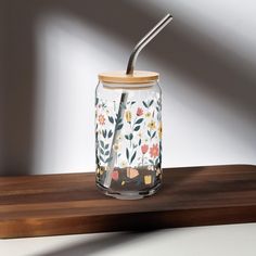 a glass jar with a straw in it sitting on a wooden table next to a white wall