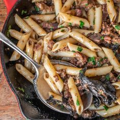 a skillet filled with pasta, meat and sauce on top of a wooden table