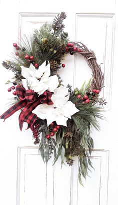 a christmas wreath with poinsettis and greenery hangs on a white door