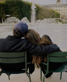 two people sitting on green chairs in front of a fountain