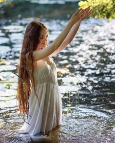 a woman in a white dress is standing in the water and holding her hands up