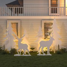 two deer standing next to each other in front of a house with christmas trees on the lawn