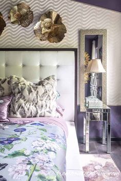 a bedroom with purple walls and floral bedding, mirrored nightstands and mirror table