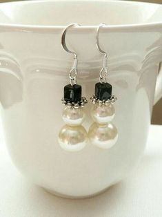 a pair of earrings with pearls and black beads on them sitting in front of a cup