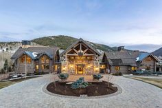 a large stone driveway leading to a log cabin style home in the mountains at dusk