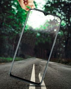 a hand holding an empty cell phone in the middle of a road with trees behind it