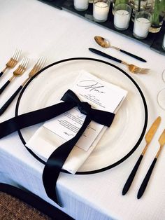 a table set with black and white place settings, silverware, and napkins