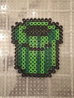 a green and black beaded skull on a gray tiled floor with white squares in the background