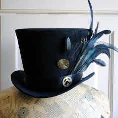 "The \"Mad as a Hatter\" is a stunning steampunk gothic top hat covered with a beautiful black flat brocade.It is lushly decorated with a variety of feathers at one side. It is further embellished with two vintage watch parts hatpins as well as a big vintage alarm clock gear! This hat is fully lined with satin and it is made to according to your exact head measurement making it suitable for both men and women who want a bit more on their head than a mini hat! IMPORTANT NOTES: -Please, make sure Feather Mohawk, Mad Hatter Top Hat, Vintage Alarm Clock, Leather Face Mask, Clock Gears, Vintage Alarm Clocks, Gothic Tops, Wonderland Costumes, Feather Tops