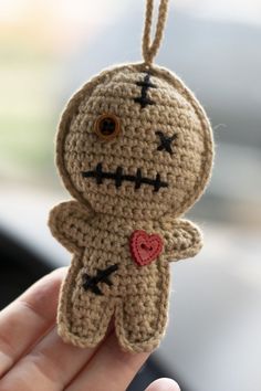 a small crocheted voodoo doll hanging from a string in someone's hand