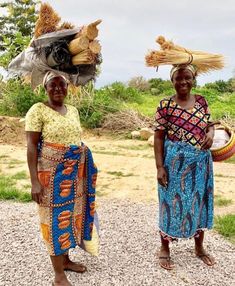 two women standing next to each other in front of grass and dirt area with trees