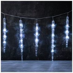 a string of lights hanging from a wire on top of a black wall with snow flakes