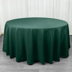 a round table with a green cloth on it in front of a white wall and wooden floor