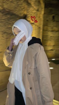 a woman walking down a street while wearing a white scarf around her neck and head