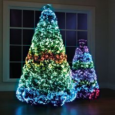 three brightly lit christmas trees in front of a window