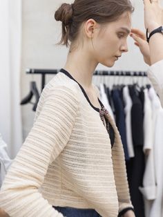 a woman is trying on her hair in front of a rack of clothes