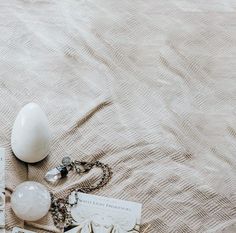 an assortment of jewelry laying on top of a bed next to a white ball and keychain