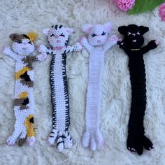 four crocheted cats laying next to each other on a white blanket with pink flowers