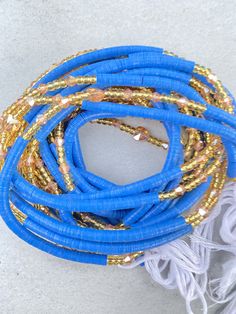 blue and gold bracelets with white tassels on the ends, sitting on a gray surface