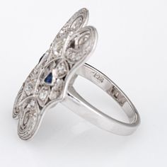 Finely detailed vintage Art Deco era diamond & sapphire ring (circa 1920s to 1930s) crafted in 14k white gold.   Two old mine cut diamonds are estimated at 0.10 carats each, accented with a further 8 estimated 0.02 carat diamonds. The total diamond weight is estimated at 0.36 carats (estimated at I-J colour and SI1-2 clarity). Two French cut sapphire total an estimated 0.06 carats.   The finely detailed Art Deco era ring features scrolled filigree with mil grain overlay details in an elongated d Vintage Diamond White Sapphire Jewelry, Vintage Sapphire Jewelry In Diamond White, Antique Silver Sapphire Ring With Diamond Accents, Art Deco Sapphire Ring For Anniversary, Art Deco Sapphire Anniversary Ring, Art Deco Sapphire Ring With Diamond Accents, Vintage Sapphire Rings With Intricate Design, Vintage Sapphire Jewelry With Intricate Design, Formal Victorian Sapphire Ring Accented With Diamonds