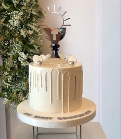 a white cake sitting on top of a table next to a green plant and a cross