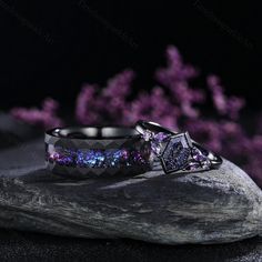 two wedding rings with purple and blue stones on top of rocks next to some pink flowers