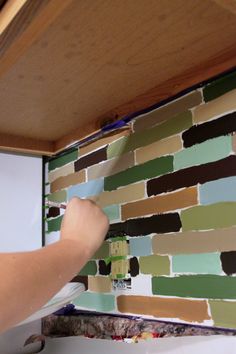 someone is painting the backsplash of a kitchen wall with multicolored tiles