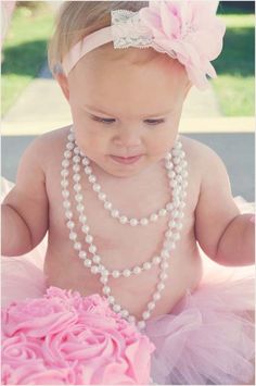 a baby wearing a pink tutu and pearls necklace