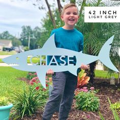 a young boy holding up a sign that says chase in front of a garden with flowers and trees