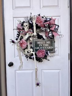 a wreath decorated with skeletons and pink flowers on the front door to a halloween themed home