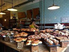 a woman standing in front of a counter filled with pastries and breads on trays