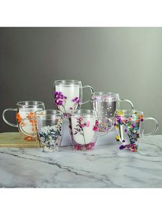 six glass mugs with flowers on them sitting on a marble counter top next to each other