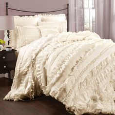 a bed with white ruffled comforter and pillows on top of it, next to a night stand