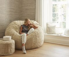 a woman sitting on a bean bag chair in front of a window with her legs crossed