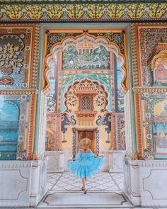 a woman in a blue dress is standing in front of an ornate wall with paintings on it