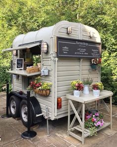 an old trailer converted into a coffee shop with potted plants and flowers on the outside