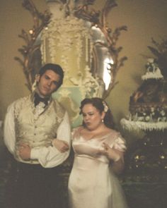 a man and woman standing next to each other in front of a fancy wall decoration