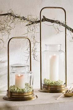 two glass jars with candles inside sitting on a table