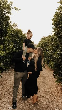 a man and woman are kissing while holding a small child in their arms as they walk through an orchard