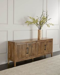 a vase with flowers sitting on top of a wooden sideboard next to a wall