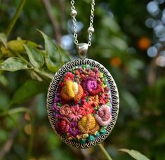 a close up of a necklace on a chain with flowers in the middle and green leaves behind it