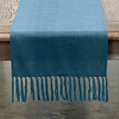 a blue table runner with tassels on it sitting on top of a wooden bench