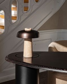 a table with a lamp on it in front of a stair case and some chairs