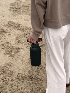 a person in white pants holding a black case on the ground with dirt and grass behind them