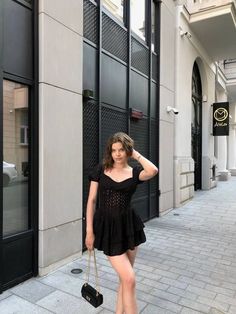 a woman is standing on the sidewalk with her hand on her head and holding a purse