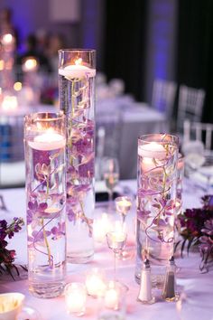 several tall vases filled with flowers and lit candles on top of a white table cloth