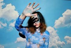 a woman with her hands up in front of a blue sky and white clouds background