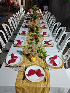 a long table with white chairs and red napkins on it is set for dinner