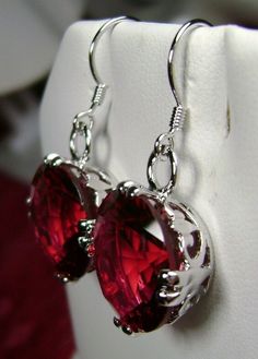 "Simulated Red Ruby Earrings F Design#E7 Made to Order This is a brand new beautiful Art Nouveau inspired filigree sterling silver pair of earrings. The gorgeous 22 carat weight captivating gems are high quality flawless man-made rubies. The lovely round full cut simulated rubies are 15mm (9/16\") in diameter. The earrings are 1-5/16\" long. Notice the beautiful fleur de lis filigree subtly designed into the settings. These are simple, elegant earrings with lovely detail. Suggested Retail $129 * Classic Red Ruby Earrings, Classic Ruby Red Earrings, Classic Red Dangle Earrings, Classic Red Earrings For Party, Red Formal Pierced Earrings, Red Pierced Earrings For Formal Occasions, Formal Red Pierced Earrings, Classic Red Party Earrings, Red Pierced Earrings For Anniversary