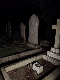 an old cemetery at night with tombstones on the ground and plants in the foreground